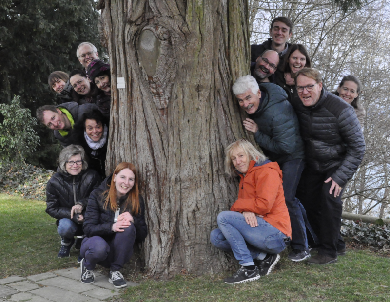 Gruppenbild seitlich halb hinter und vor einm Baumstamm